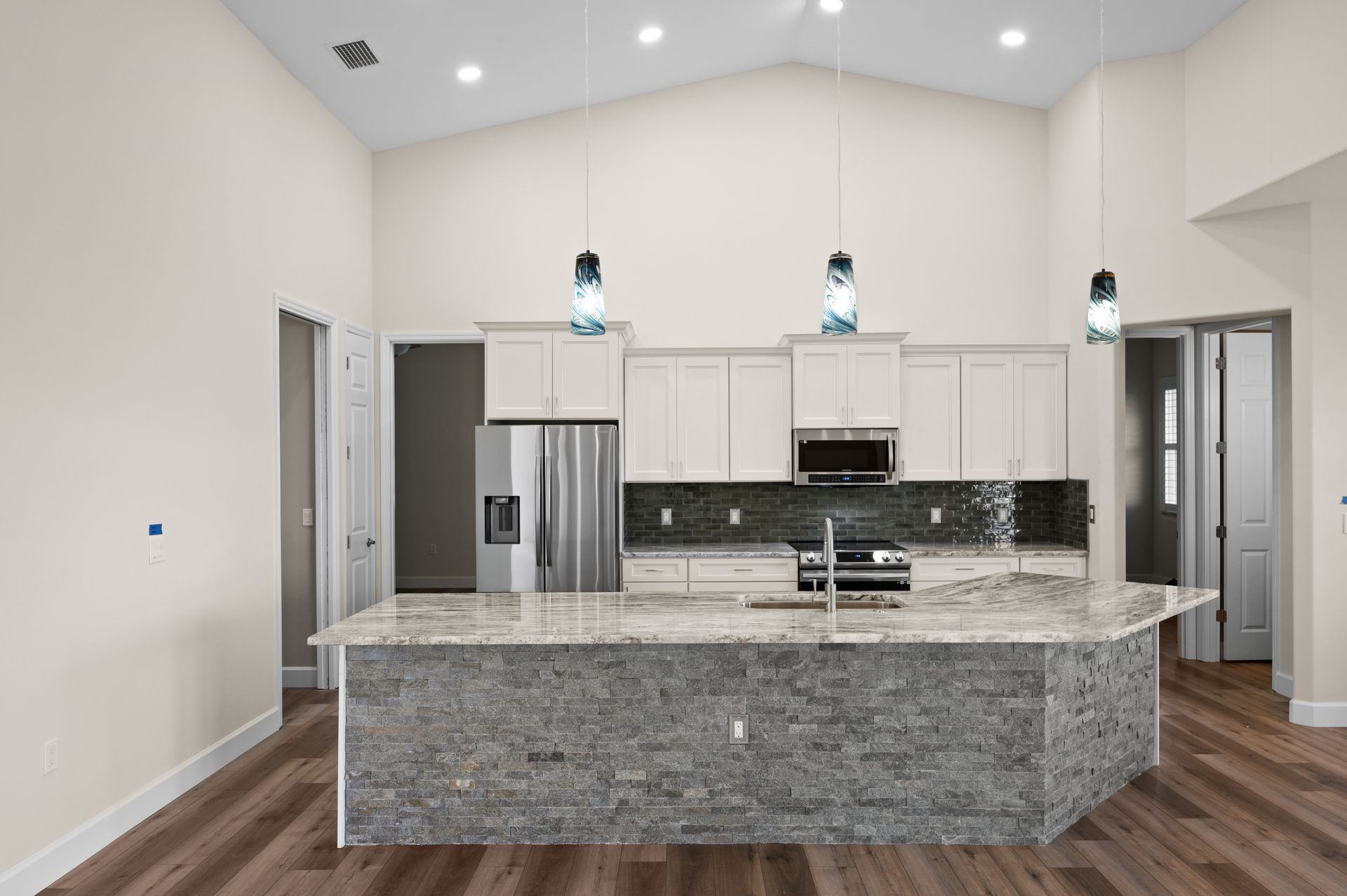 Modern kitchen with a large stone island, white cabinets, and pendant lights.