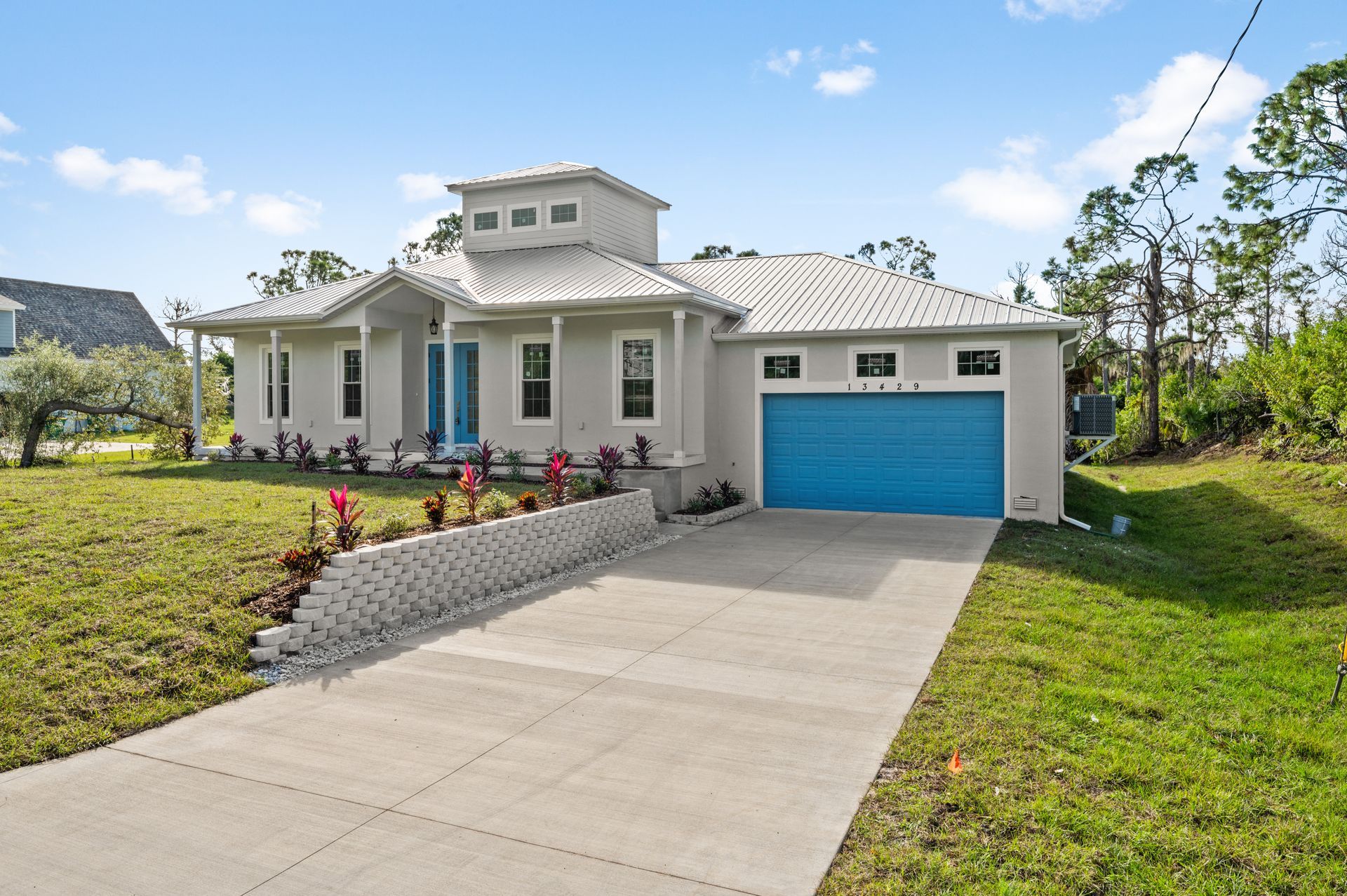 Light gray house with turquoise door and garage, on a slightly sloped lot with a concrete driveway.