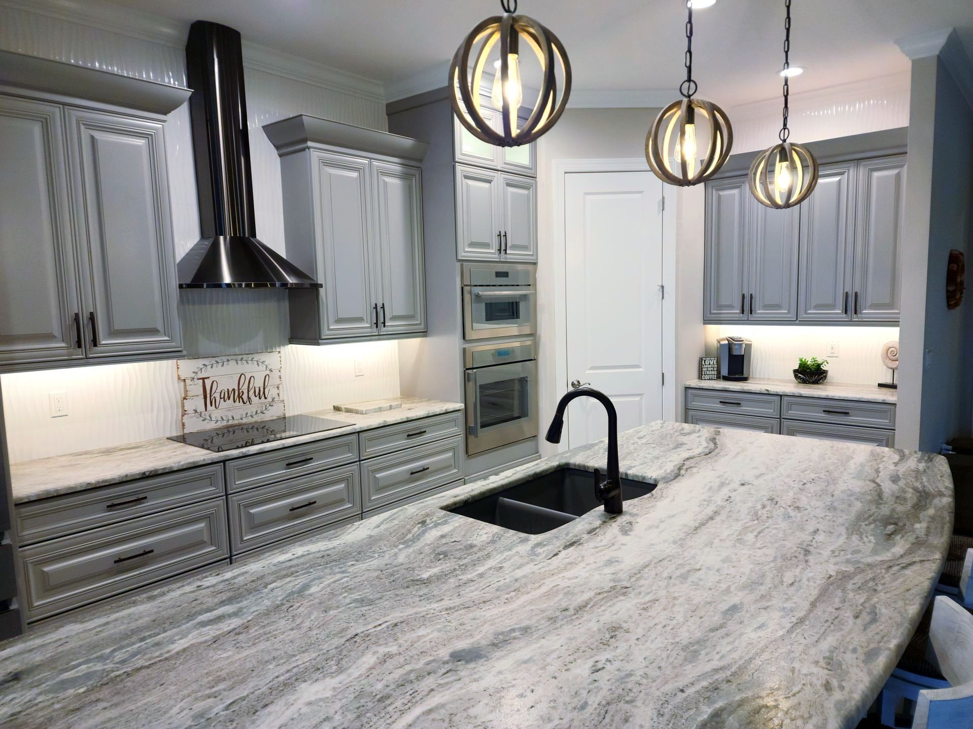 Gray kitchen with marble island and light fixtures.