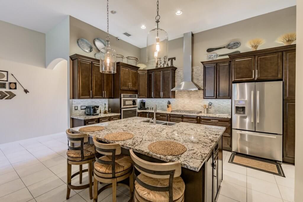 Kitchen with dark cabinets, large granite island, stainless steel appliances, and stools.