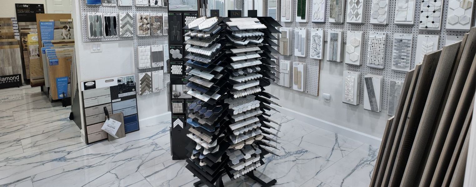 A well-lit showroom features a central tower of tile samples surrounded by wall-mounted and floor-standing flooring options.