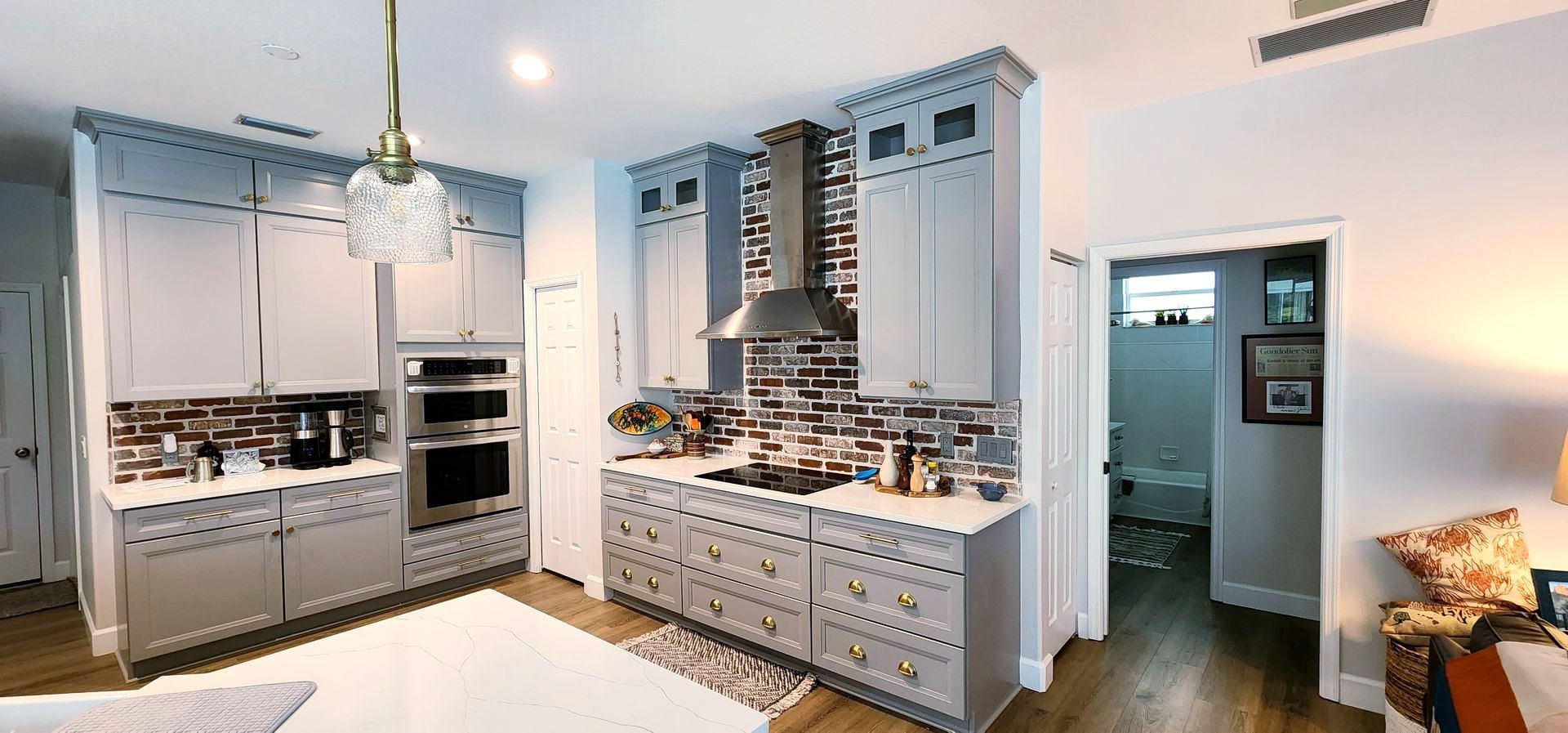 Gray kitchen with brick backsplash, overhead lighting, and doorway to the bathroom.